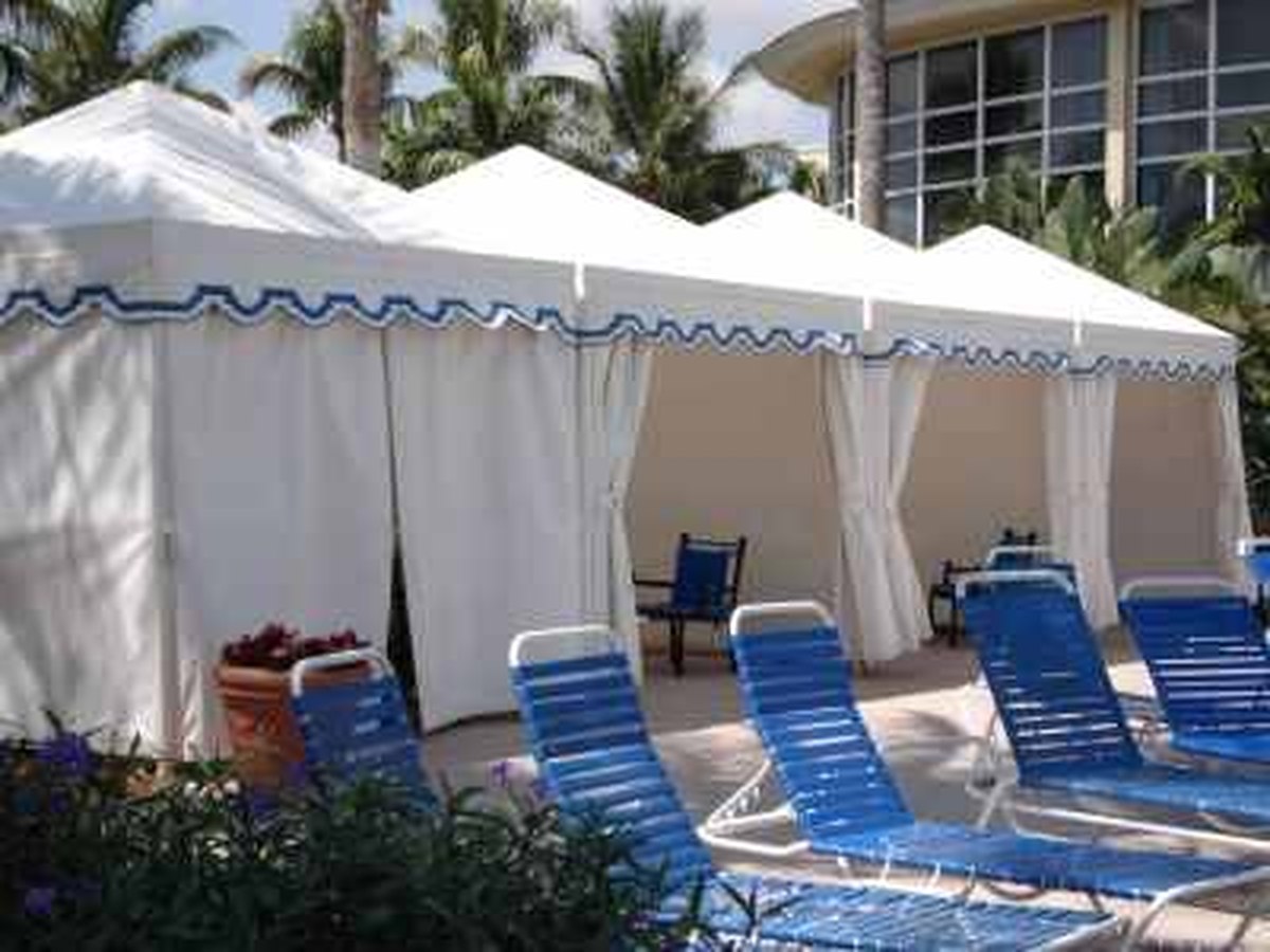Row of white-and-navy striped resort poolside cabanas with blue striped lounge chairs and palm trees on a sunny South Florida afternoon.