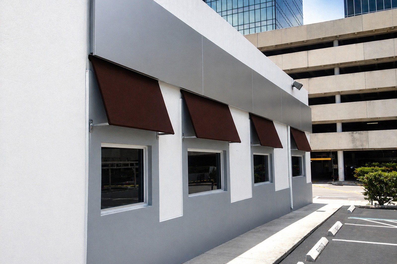 Side elevation of a Brickell low-rise with four matching burgundy projecting window awnings on a clean grey-and-white commercial facade.