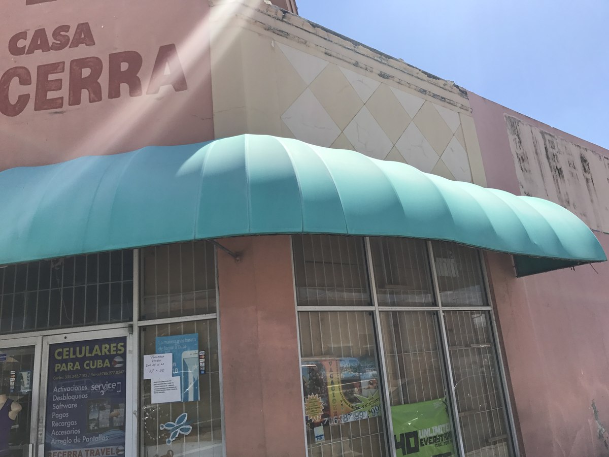 Long teal scallop-trimmed awning runs across the storefront of Casa Becerra and Becerra Travel agency on a pink stucco strip facade.