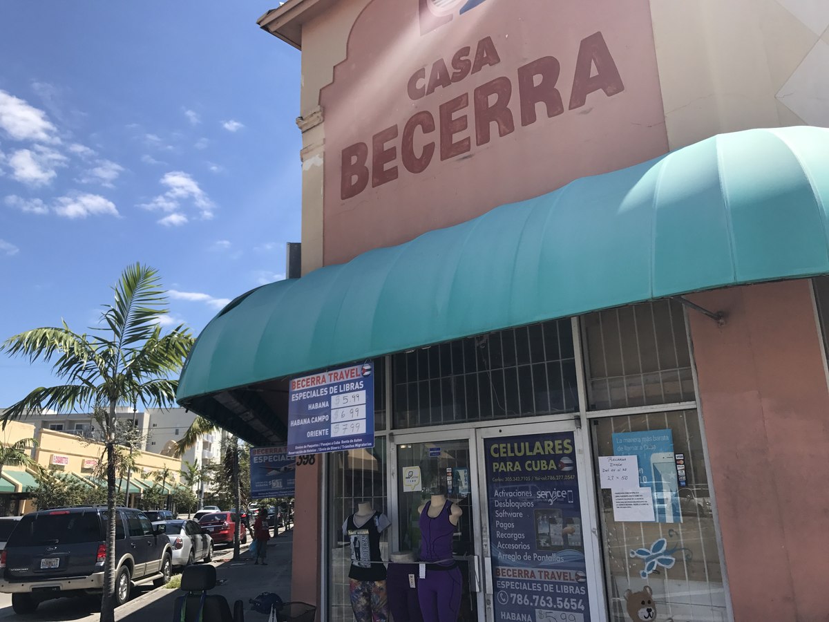 Casa Becerra storefront with teal scalloped awning, palm trees and parked cars on a busy Hialeah street, mannequins in window display.