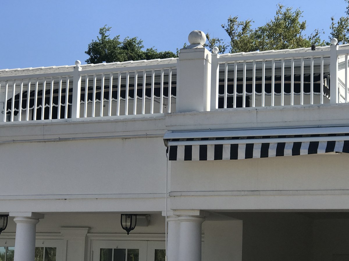 Black-and-white scalloped awnings over second-story balcony and ground-level columns on an upscale white classic home.