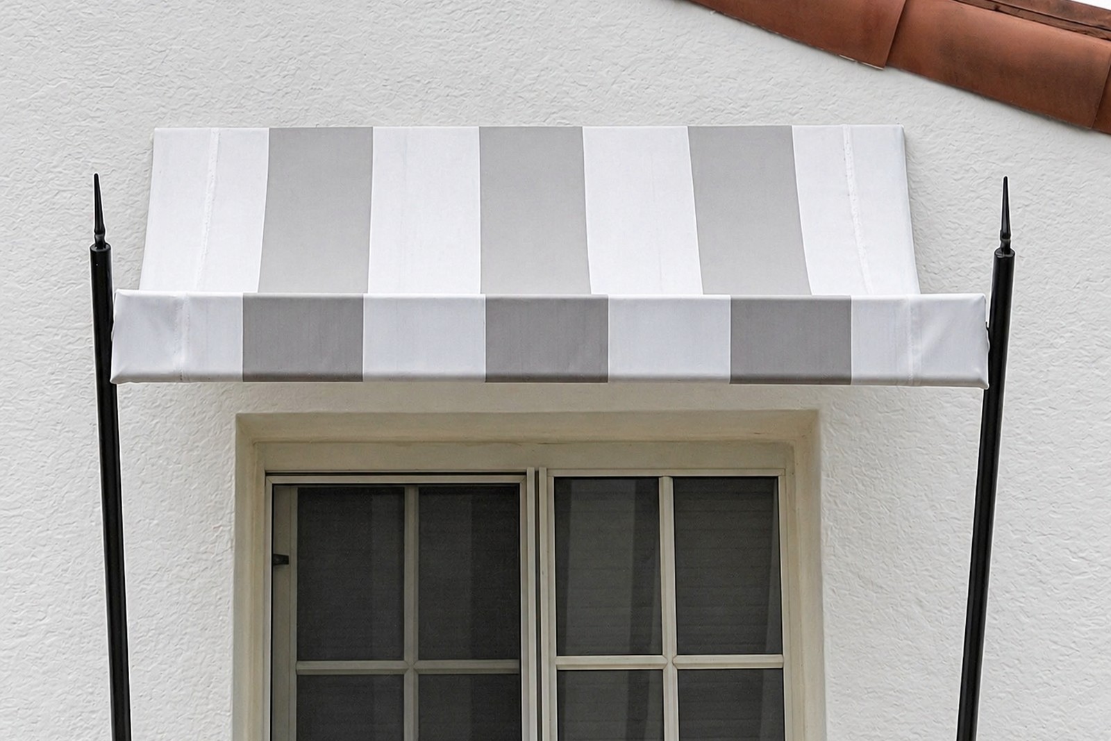 Crisp grey-and-white striped fabric window awning bracketed by black wrought-iron finials on a white stucco home with terra-cotta tile roof.