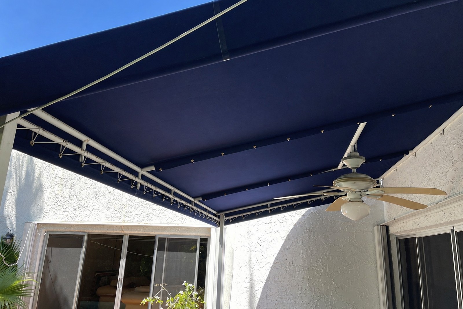 Underside of a large navy retractable awning over a screened lanai with ceiling fan and sliding-glass door.