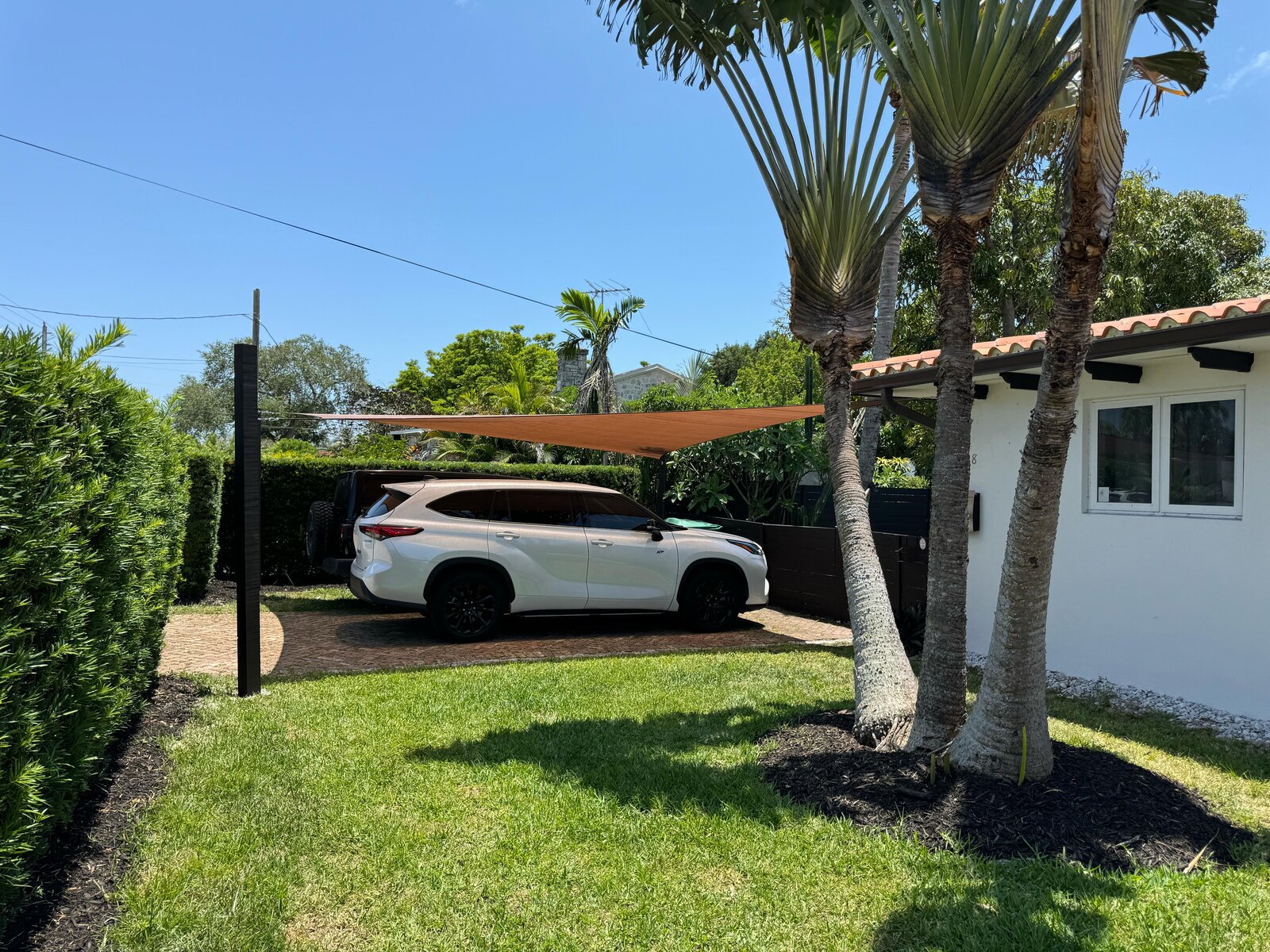 Side view of a tan shade sail attached to a tile-roof Florida home, covering a driveway